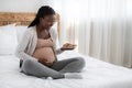 Happy pregnant woman with plate of cookies sitting in bed at home Royalty Free Stock Photo