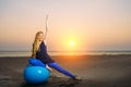 Happy pregnant woman sits on the exercise ball against sunset over the sea. Pregnancy, sport, fitness and healthy lifestyle Royalty Free Stock Photo