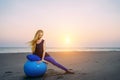 Happy pregnant woman sits on the exercise ball against sunset over the sea. Pregnancy, sport, fitness and healthy lifestyle Royalty Free Stock Photo