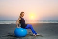 Happy pregnant woman sits on the exercise ball against sunset over the sea. Pregnancy, sport, fitness and healthy lifestyle Royalty Free Stock Photo