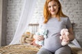 Happy pregnant woman sitting on bed at bedroom holding two cute bear toys awaiting twins baby Royalty Free Stock Photo
