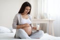 Happy pregnant woman sitting on bed, holding glass of milk Royalty Free Stock Photo