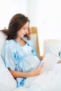 Happy pregnant woman sitting on bed reading book at home Royalty Free Stock Photo