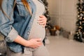 Happy pregnant woman sitting on bed and touching her belly at home over christmas tree Royalty Free Stock Photo
