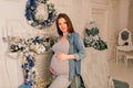 Happy pregnant woman sitting on bed and touching her belly at home over christmas tree Royalty Free Stock Photo