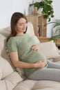 Happy pregnant woman sitting on sofa and touching her belly in living room Royalty Free Stock Photo