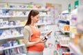 Happy pregnant woman with smartphone at pharmacy