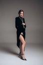 Happy pregnant woman stands and smiles in black dress with beads in studio against dark background