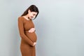 Happy pregnant woman touching her abdomen at Colored background. Future mother is wearing white underwear. Expecting of Royalty Free Stock Photo