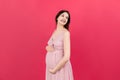 Happy pregnant woman touching her abdomen at Colored background. Future mother is wearing white underwear. Expecting of Royalty Free Stock Photo