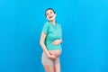 Happy pregnant woman touching her abdomen at Colored background. Future mother is wearing white underwear. Expecting of a baby. Royalty Free Stock Photo