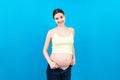 Happy pregnant woman in unzipped jeans showing her abdomen at colorful background with copy space Royalty Free Stock Photo