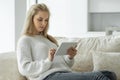 Happy pregnant woman uses a digital tablet while sitting on the sofa in the living room Royalty Free Stock Photo