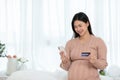 Happy pregnant woman using credit card shopping online at home.Mother purchasing baby clothes from internet online store by mobile Royalty Free Stock Photo