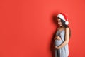 Happy pregnant woman wearing Santa hat for Christmas party on red background. Expecting baby Royalty Free Stock Photo