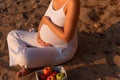 Happy pregnant woman with white clothes touching her belly with love on sunset beach Royalty Free Stock Photo