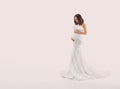 Happy pregnant woman in white dress gently hugs touch her belly with hands. Light beige studio background. Beautiful Royalty Free Stock Photo