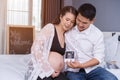 Happy pregnant woman and her husband holding ultrasound scan photo on bed Royalty Free Stock Photo