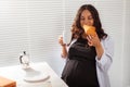 Happy pregnant young beautiful woman eating croissant during morning breakfast. Concept of pleasant morning and positive Royalty Free Stock Photo