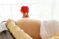 Happy pregnant young woman holding red heart in hand on top of mother belly in hospital bed. prenatal, pregnancy, motherhood,