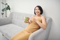 Happy pregnant young woman sitting and eating salad on sofa at home Royalty Free Stock Photo