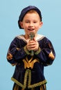 Happy preschool age boy in costume of medieval pageboy, little prince singing at microphone over light blue background Royalty Free Stock Photo