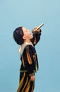 Happy preschool age boy in costume of medieval pageboy, little prince singing at microphone over light blue background Royalty Free Stock Photo