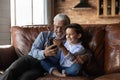 Happy preschooler boy and mature senior 70s grandpa using smartphone