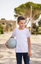 Happy preschooler boy in white t-shirt holding ball outdoors. Shirt mockup