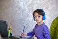 Happy preteen boy sitting on the couch or desk while using a laptop and headphones at home. Online chatting with his school Royalty Free Stock Photo