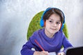 Happy preteen boy sitting on the couch or desk while using a laptop and headphones at home. Online chatting with his school Royalty Free Stock Photo