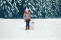 Happy preteen boy walking with his white Samoyed dog in winter snowy day over trees forest