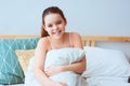happy preteen girl sitting on bed and hugs cozy pillow