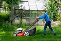 Happy preteen kid boy with lawn mower. Portrait of smiling teenager child working in garden, trimming grass. Garden works in Royalty Free Stock Photo