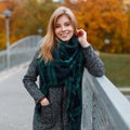 Happy pretty cute young woman in a vintage autumn stylish coat in a fashionable green scarf is standing outdoors