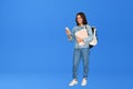 Happy girl student holding backpack using smartphone isolated on blue. Royalty Free Stock Photo