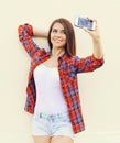 Happy pretty girl wear a checkered red shirt and shorts makes self-portrait on the smartphone Royalty Free Stock Photo