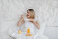 Happy pretty hungry young european blonde woman wake up, have breakfast in white bed Royalty Free Stock Photo