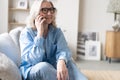 Happy mature woman speaking on smartphone. Senior grey haired lady making telephone call, sitting on couch at home Royalty Free Stock Photo