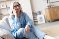 Happy mature woman speaking on smartphone. Senior grey haired lady making telephone call, sitting on couch at home Royalty Free Stock Photo