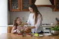 Happy pretty mom teaching girl to cook salad in kitchen Royalty Free Stock Photo