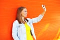 Happy pretty smiling woman makes self-portrait on smartphone over colorful orange Royalty Free Stock Photo