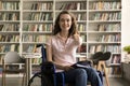 Happy pretty student girl using wheelchair, posing in library Royalty Free Stock Photo