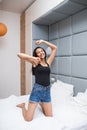 Happy pretty woman in earphones listening to music and singing and dance while sitting on bed and holding mobile phone Royalty Free Stock Photo