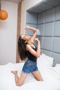 Happy pretty woman in earphones listening to music and singing and dance while sitting on bed and holding mobile phone Royalty Free Stock Photo