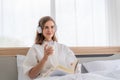Happy pretty woman in earphones listening to music and singing while sitting on bed Royalty Free Stock Photo