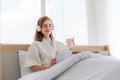 Happy pretty woman in earphones listening to music and singing while sitting on bed Royalty Free Stock Photo