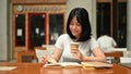 A happy Asian woman reading a book, doing homework and sipping coffee at a coffee shop Royalty Free Stock Photo