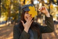 Happy pretty young attractive woman with a smile in a fashionable coat and hat covers her face with her hand and a yellow autumn. Royalty Free Stock Photo