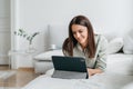 Happy pretty young woman in casual outfit sitting on sofa at home and using tablet while browsing internet Royalty Free Stock Photo